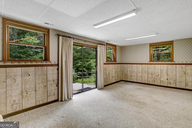 unfurnished room with wood walls, a drop ceiling, and light colored carpet