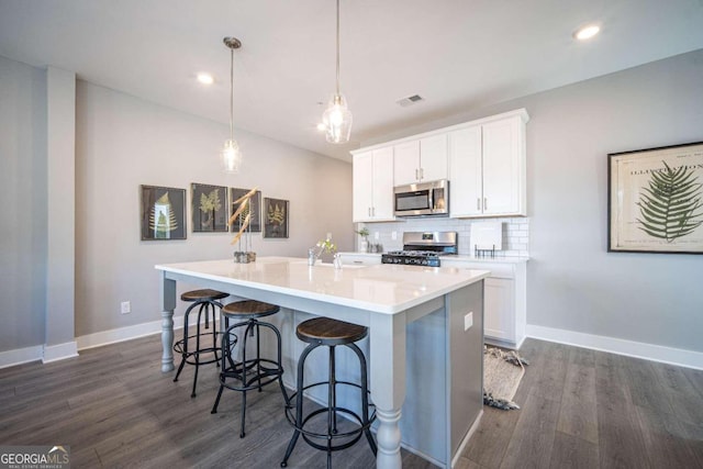 kitchen with pendant lighting, a kitchen island with sink, stainless steel appliances, and white cabinets