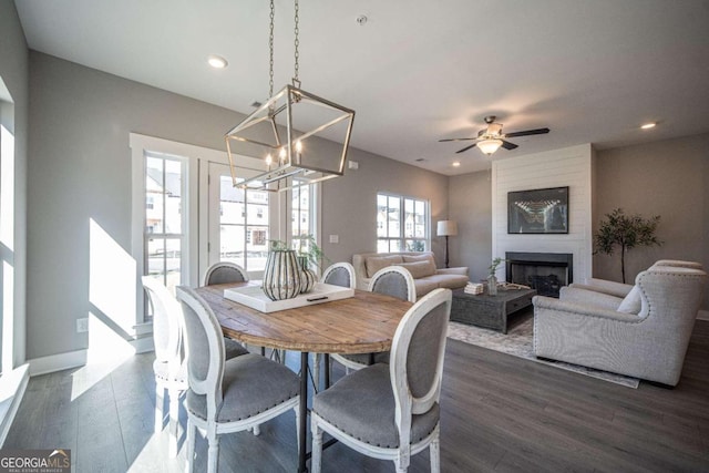 dining space with dark wood-type flooring, a fireplace, and ceiling fan with notable chandelier