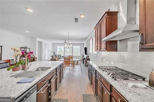 kitchen with pendant lighting, stainless steel appliances, light stone counters, and wall chimney range hood