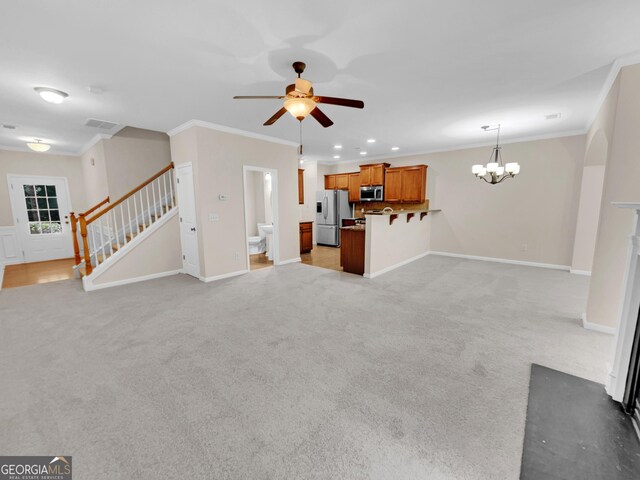 unfurnished living room with light carpet, ceiling fan with notable chandelier, and ornamental molding