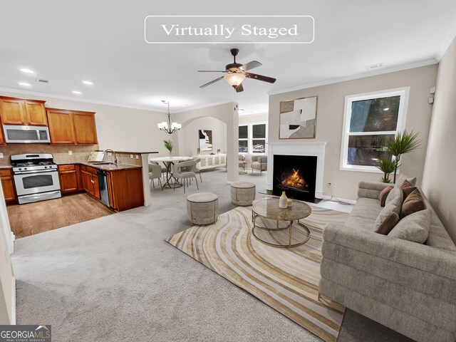 living room with ceiling fan with notable chandelier, light colored carpet, ornamental molding, and sink