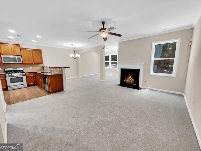 unfurnished living room featuring ceiling fan with notable chandelier, light colored carpet, ornamental molding, and sink