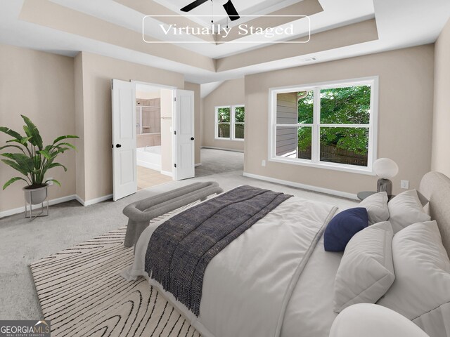 carpeted bedroom featuring a raised ceiling, ceiling fan, and ensuite bathroom