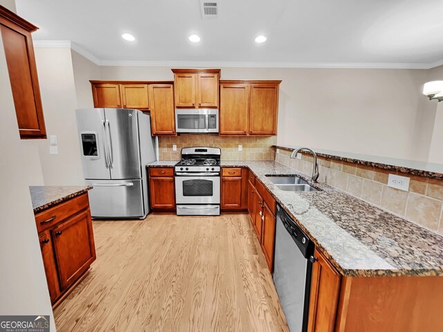 kitchen featuring sink, decorative backsplash, light stone countertops, light wood-type flooring, and appliances with stainless steel finishes