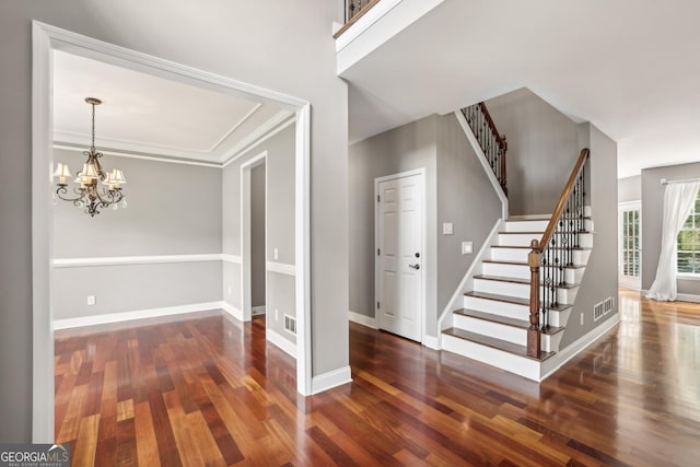 foyer entrance featuring a notable chandelier, ornamental molding, and dark wood-type flooring