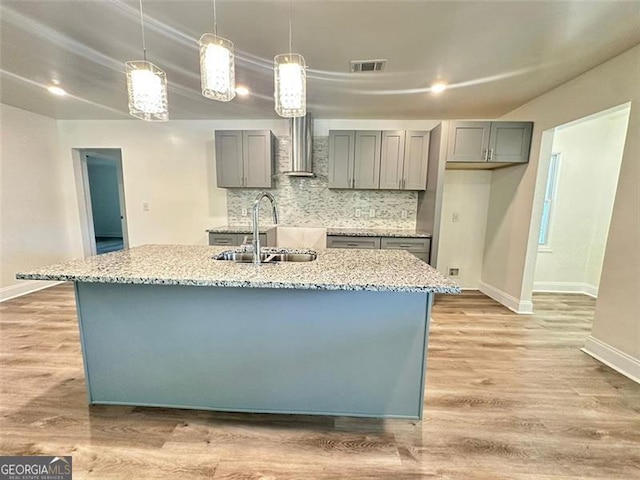 kitchen featuring an island with sink, light hardwood / wood-style floors, sink, and wall chimney exhaust hood