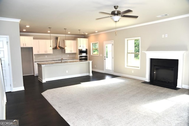 kitchen featuring pendant lighting, white cabinetry, a kitchen island with sink, and wall chimney exhaust hood