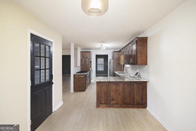 kitchen featuring kitchen peninsula, backsplash, dark brown cabinets, sink, and stainless steel refrigerator