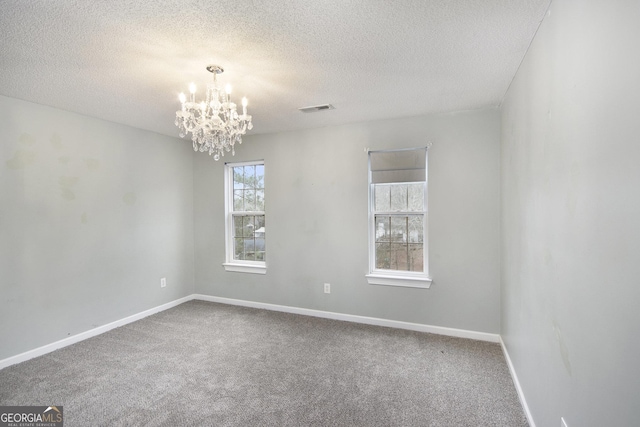 spare room with carpet, a textured ceiling, and a notable chandelier