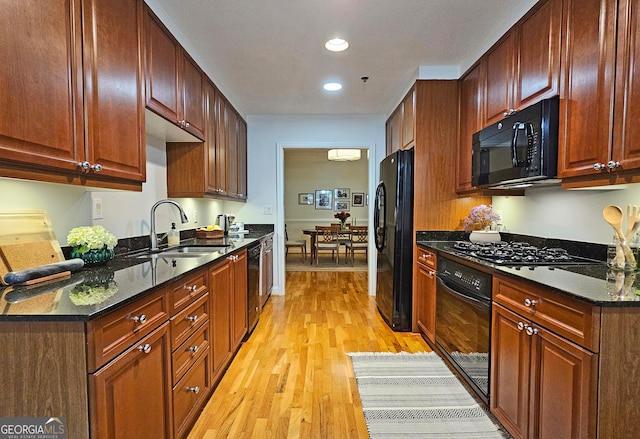 kitchen featuring dark stone countertops, sink, black appliances, and light wood-type flooring