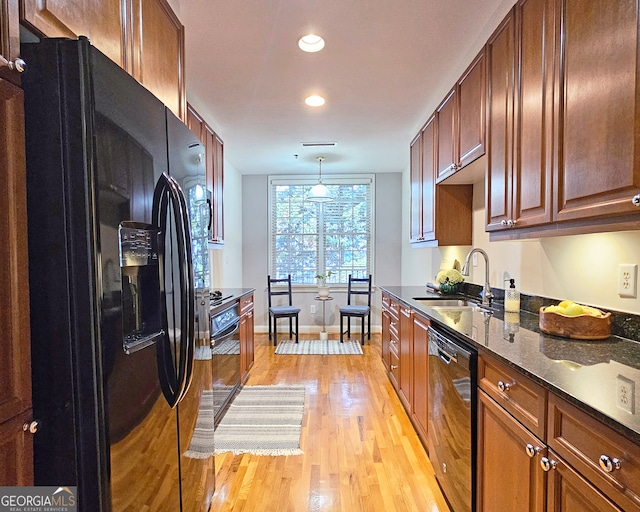 kitchen with light hardwood / wood-style flooring, pendant lighting, black appliances, dark stone countertops, and sink