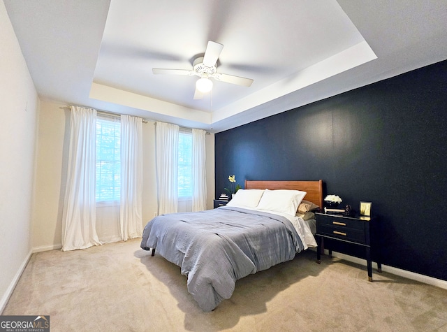 carpeted bedroom featuring ceiling fan and a raised ceiling