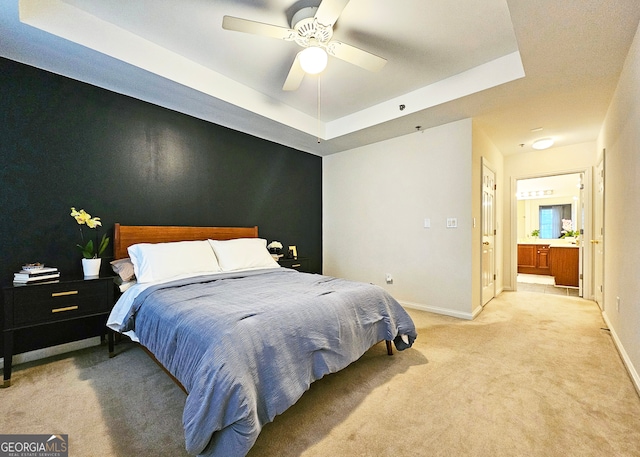 carpeted bedroom with ceiling fan, a raised ceiling, and connected bathroom