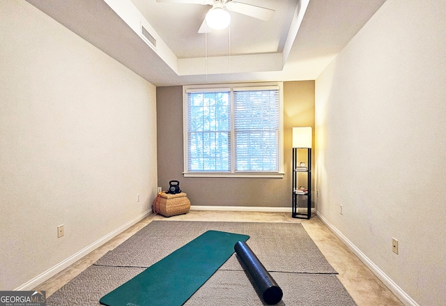 exercise area with ceiling fan and a raised ceiling