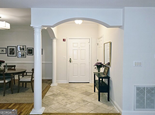 entryway featuring an AC wall unit, ornamental molding, light tile flooring, and ornate columns