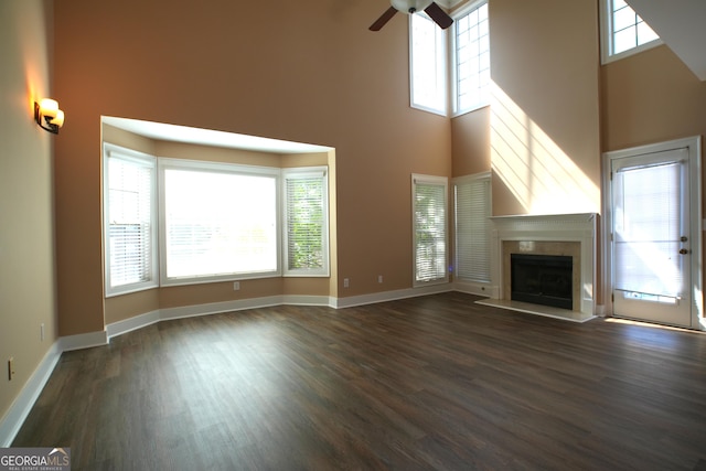 unfurnished living room with dark hardwood / wood-style flooring, ceiling fan, a fireplace, and a high ceiling