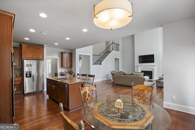 kitchen with sink, dark hardwood / wood-style floors, stainless steel appliances, light stone countertops, and a kitchen island with sink