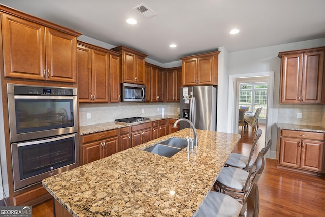 kitchen with tasteful backsplash, sink, a kitchen bar, a kitchen island with sink, and stainless steel appliances