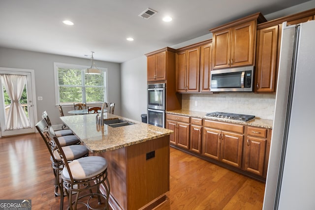 kitchen featuring appliances with stainless steel finishes, an island with sink, sink, backsplash, and hanging light fixtures