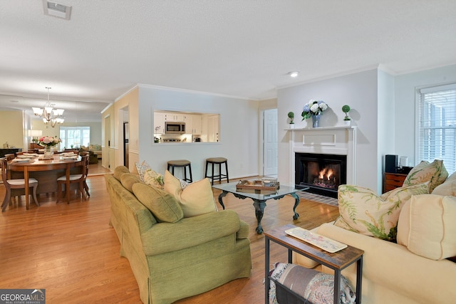 living room with ornamental molding, a healthy amount of sunlight, a notable chandelier, and light hardwood / wood-style floors