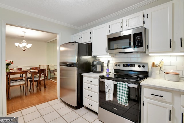 kitchen with pendant lighting, an inviting chandelier, appliances with stainless steel finishes, light tile patterned flooring, and white cabinetry