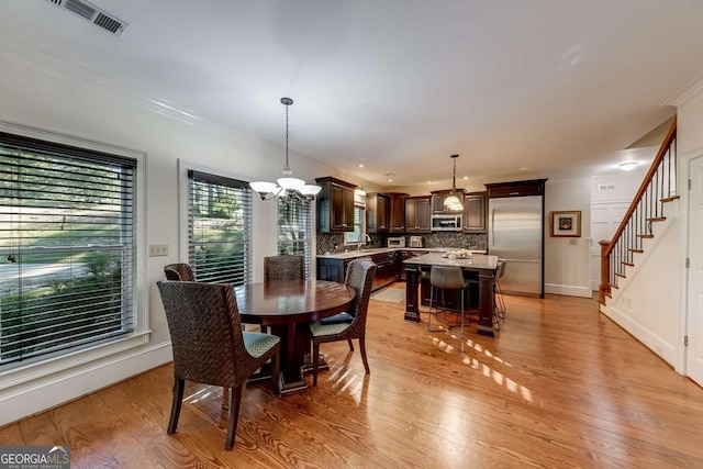 dining room with sink, ornamental molding, a chandelier, and light wood-type flooring