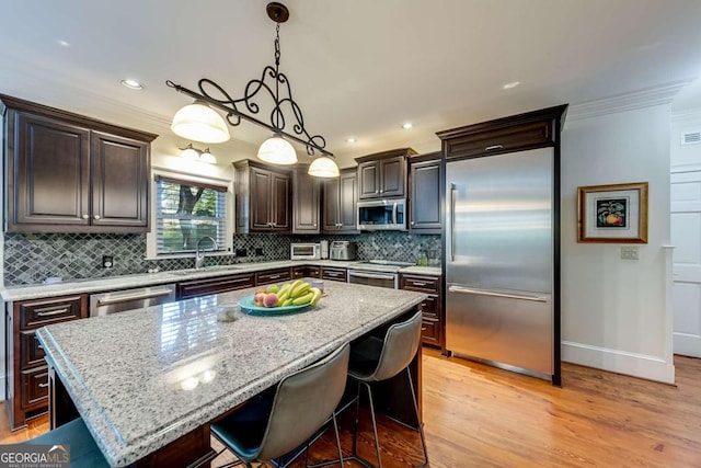 kitchen with appliances with stainless steel finishes, pendant lighting, sink, ornamental molding, and a center island