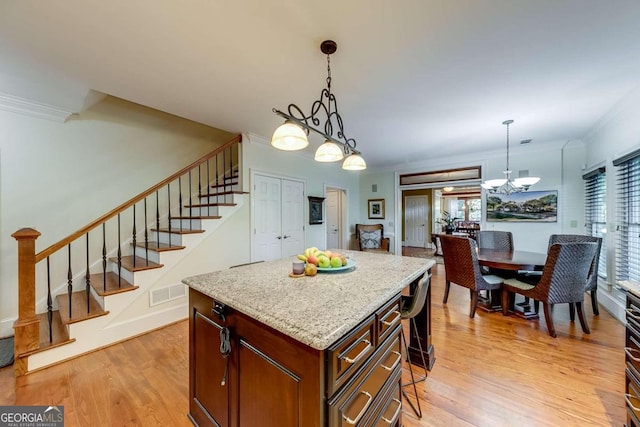 kitchen with pendant lighting, a center island, crown molding, light stone countertops, and light hardwood / wood-style flooring