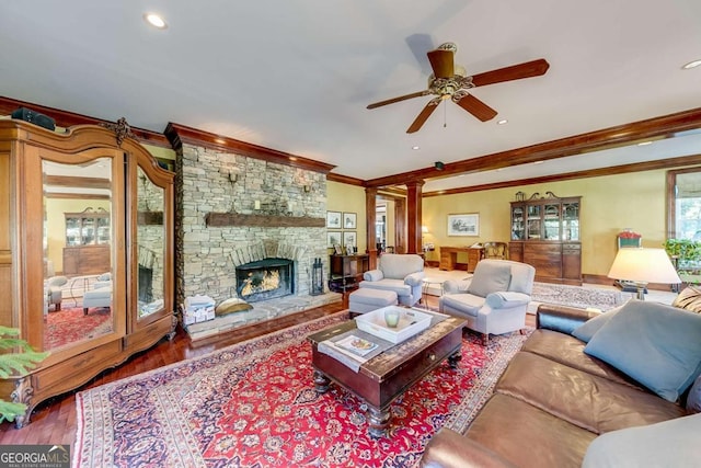 living room featuring crown molding, ceiling fan, hardwood / wood-style floors, decorative columns, and a stone fireplace