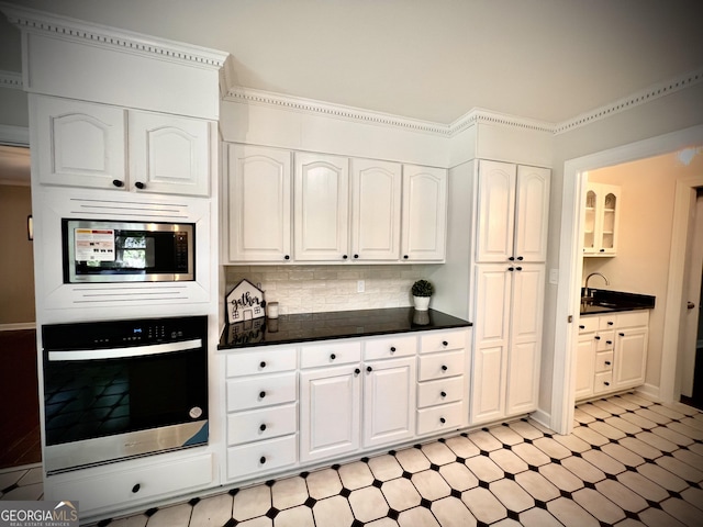 kitchen with crown molding, stainless steel microwave, backsplash, white cabinets, and oven