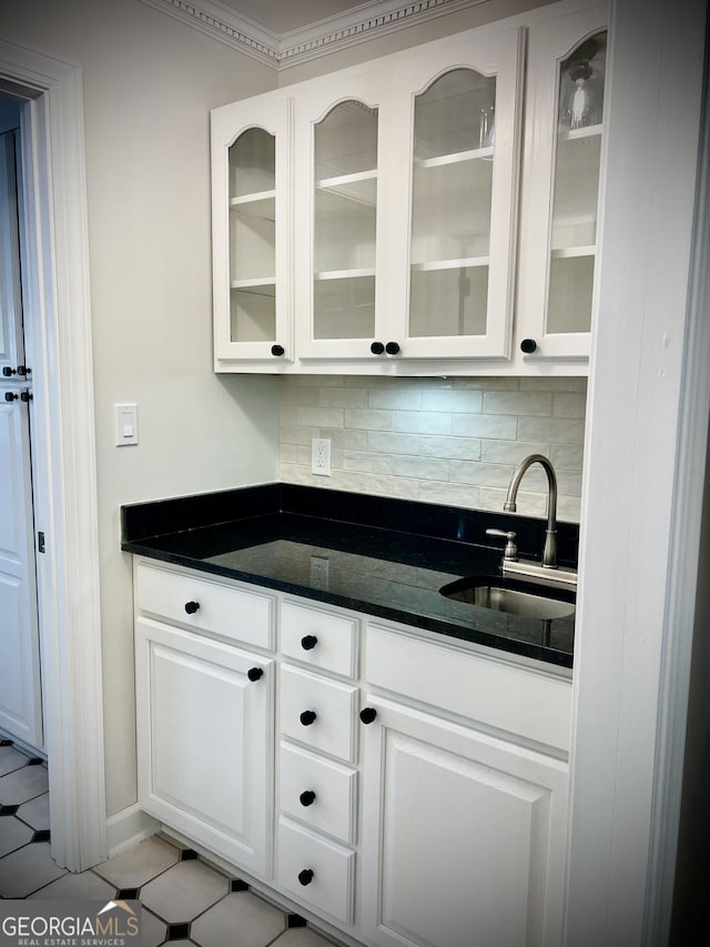 bar with tasteful backsplash, white cabinetry, light tile patterned floors, sink, and dark stone counters