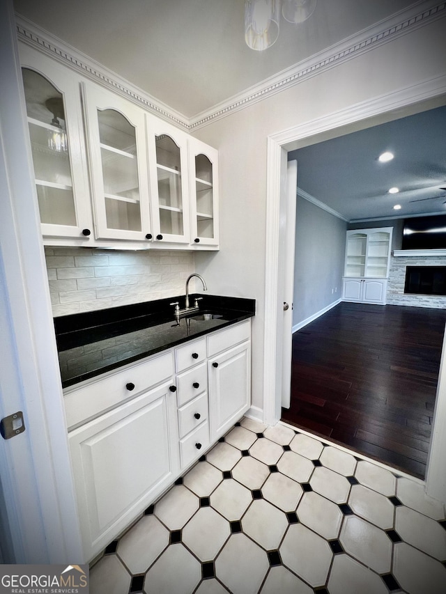 kitchen with a stone fireplace, tasteful backsplash, white cabinetry, sink, and ornamental molding