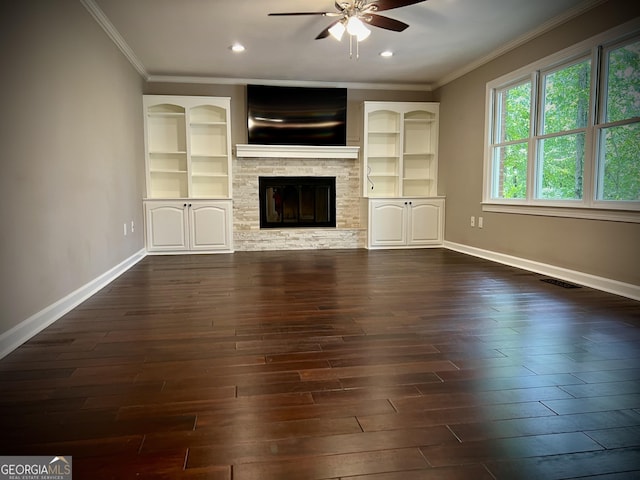 unfurnished living room with ceiling fan, a stone fireplace, ornamental molding, and dark hardwood / wood-style flooring