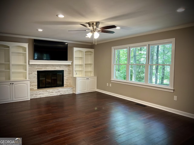 unfurnished living room with ceiling fan, dark hardwood / wood-style floors, crown molding, and a stone fireplace