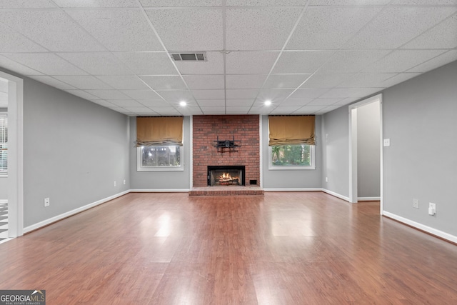 unfurnished living room with a fireplace, brick wall, hardwood / wood-style flooring, and a drop ceiling