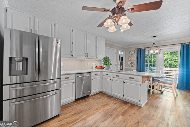 kitchen with white cabinetry, stainless steel appliances, ceiling fan with notable chandelier, crown molding, and light wood-type flooring