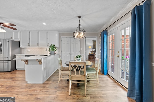 dining room featuring ceiling fan with notable chandelier, crown molding, light wood-type flooring, and a textured ceiling