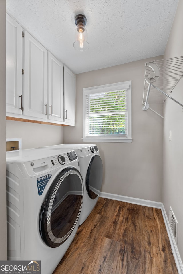 clothes washing area with cabinets, a textured ceiling, dark hardwood / wood-style floors, and washing machine and clothes dryer