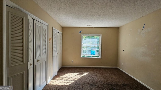 unfurnished bedroom with carpet floors, a textured ceiling, and multiple closets