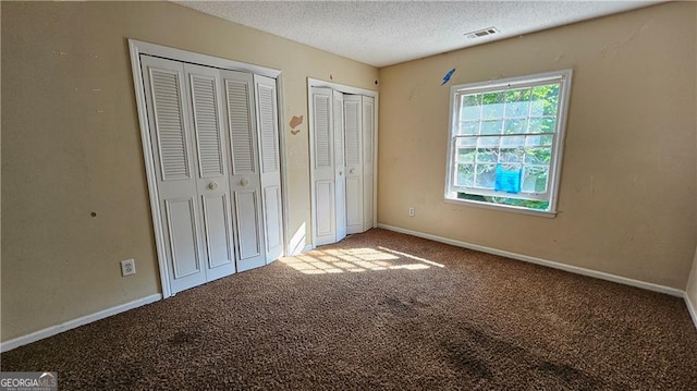 unfurnished bedroom with carpet flooring, a textured ceiling, and two closets