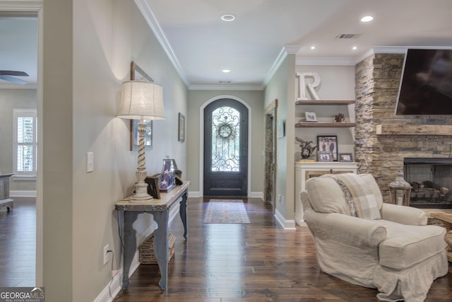 foyer with crown molding, a stone fireplace, and dark wood-type flooring