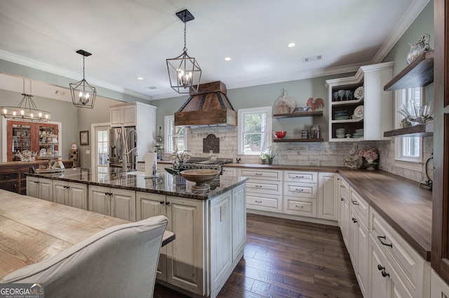 kitchen with dark wood-type flooring, stainless steel fridge, tasteful backsplash, decorative light fixtures, and custom range hood