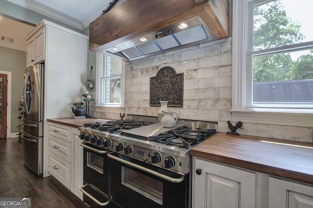 kitchen featuring custom range hood, appliances with stainless steel finishes, butcher block counters, and a healthy amount of sunlight