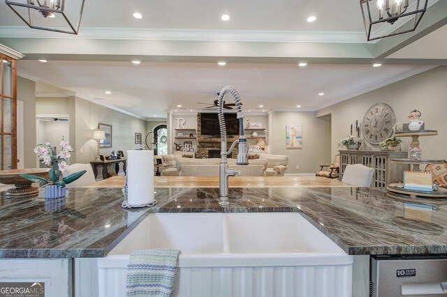 kitchen featuring ornamental molding, a stone fireplace, dark stone counters, and sink