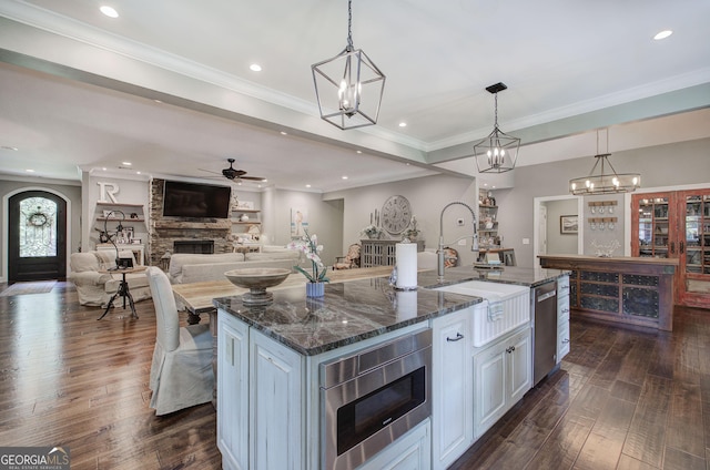 kitchen featuring a kitchen island with sink, dark stone counters, white cabinets, a stone fireplace, and stainless steel appliances