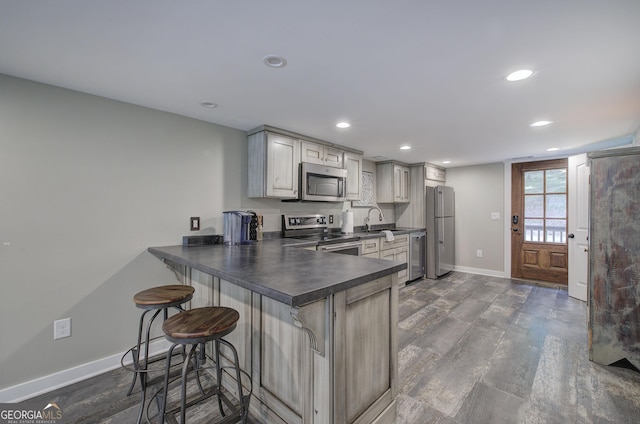 kitchen with sink, stainless steel appliances, a kitchen breakfast bar, dark hardwood / wood-style floors, and kitchen peninsula