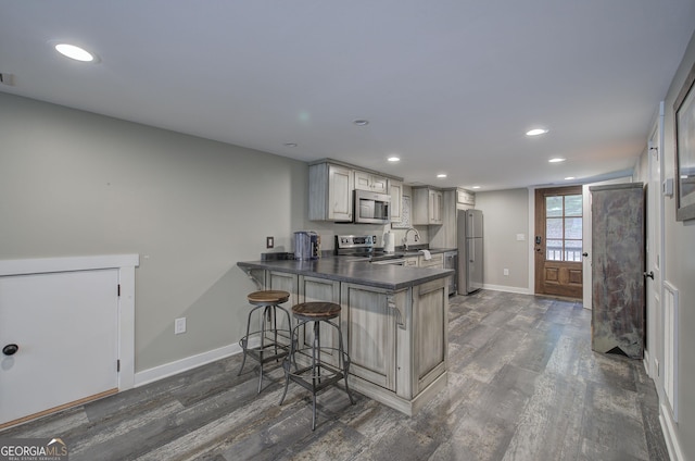 kitchen with sink, a kitchen breakfast bar, dark hardwood / wood-style flooring, kitchen peninsula, and appliances with stainless steel finishes