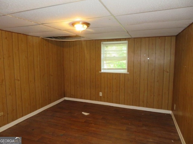 empty room featuring wood walls, a drop ceiling, and dark hardwood / wood-style floors