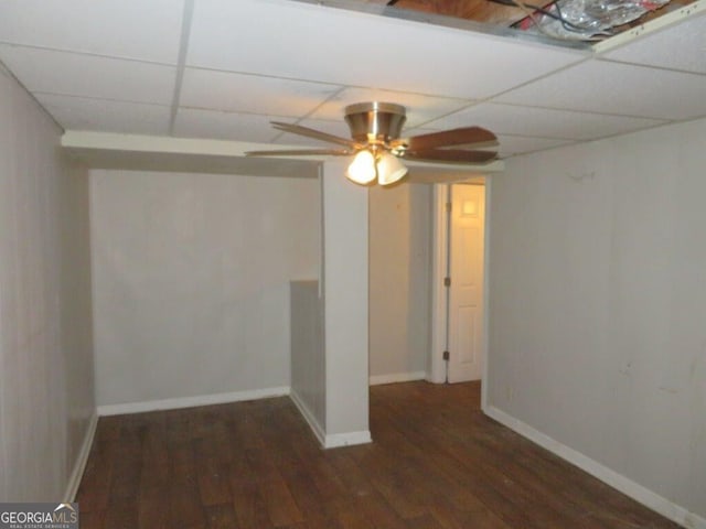 basement featuring a paneled ceiling, ceiling fan, and dark wood-type flooring